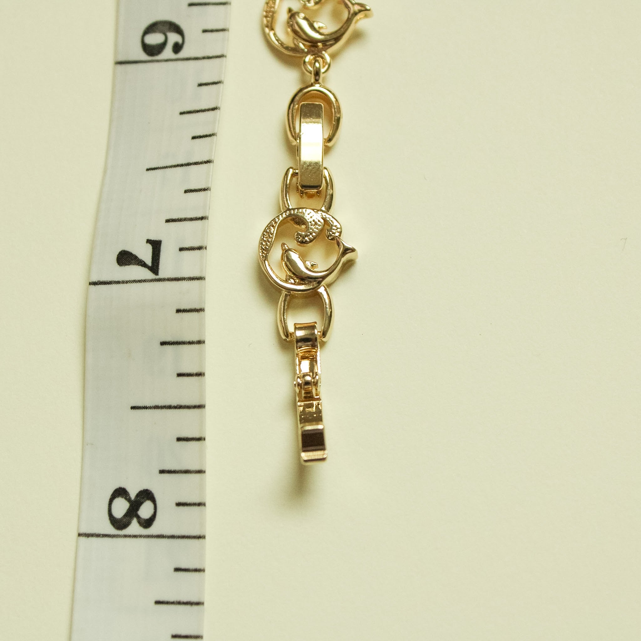 Gold-plated dolphin charm bracelet close-up of connector and bar clasp.