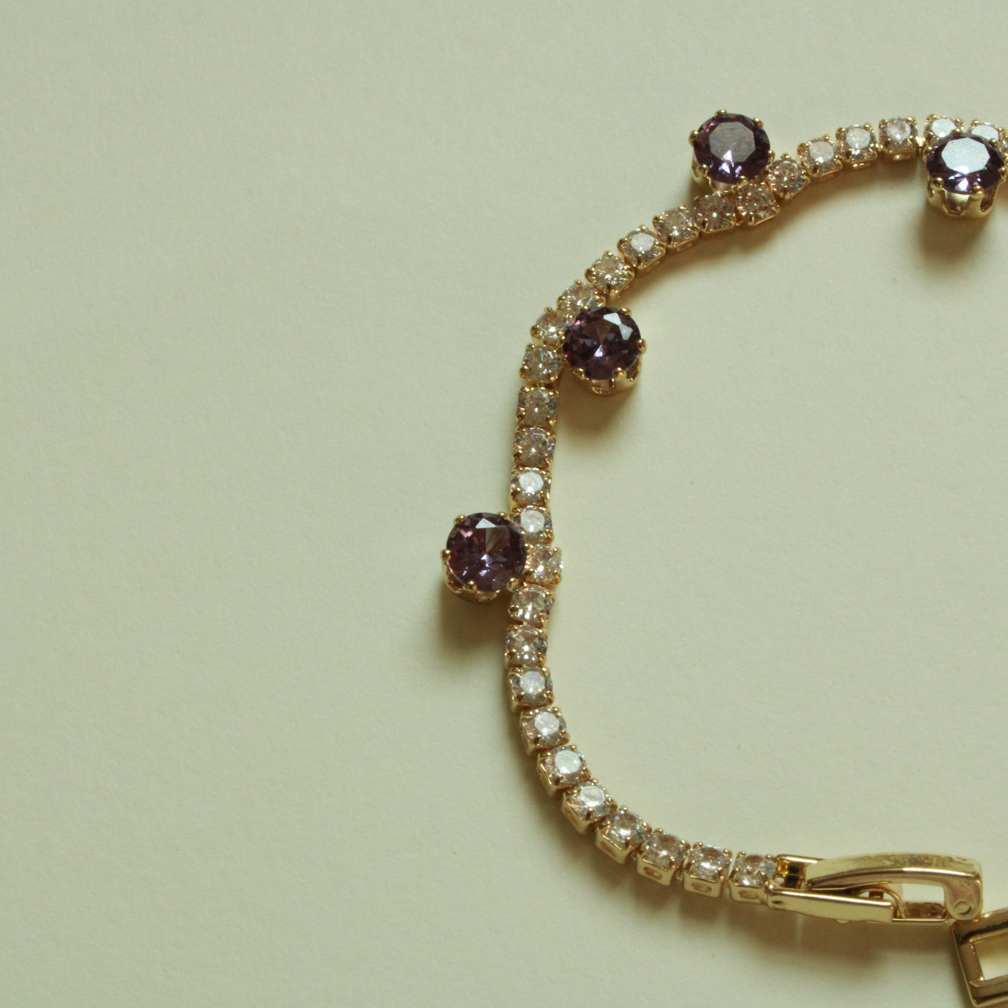Gold-plated tennis bracelet angled view with purple CZ stations and box clasp