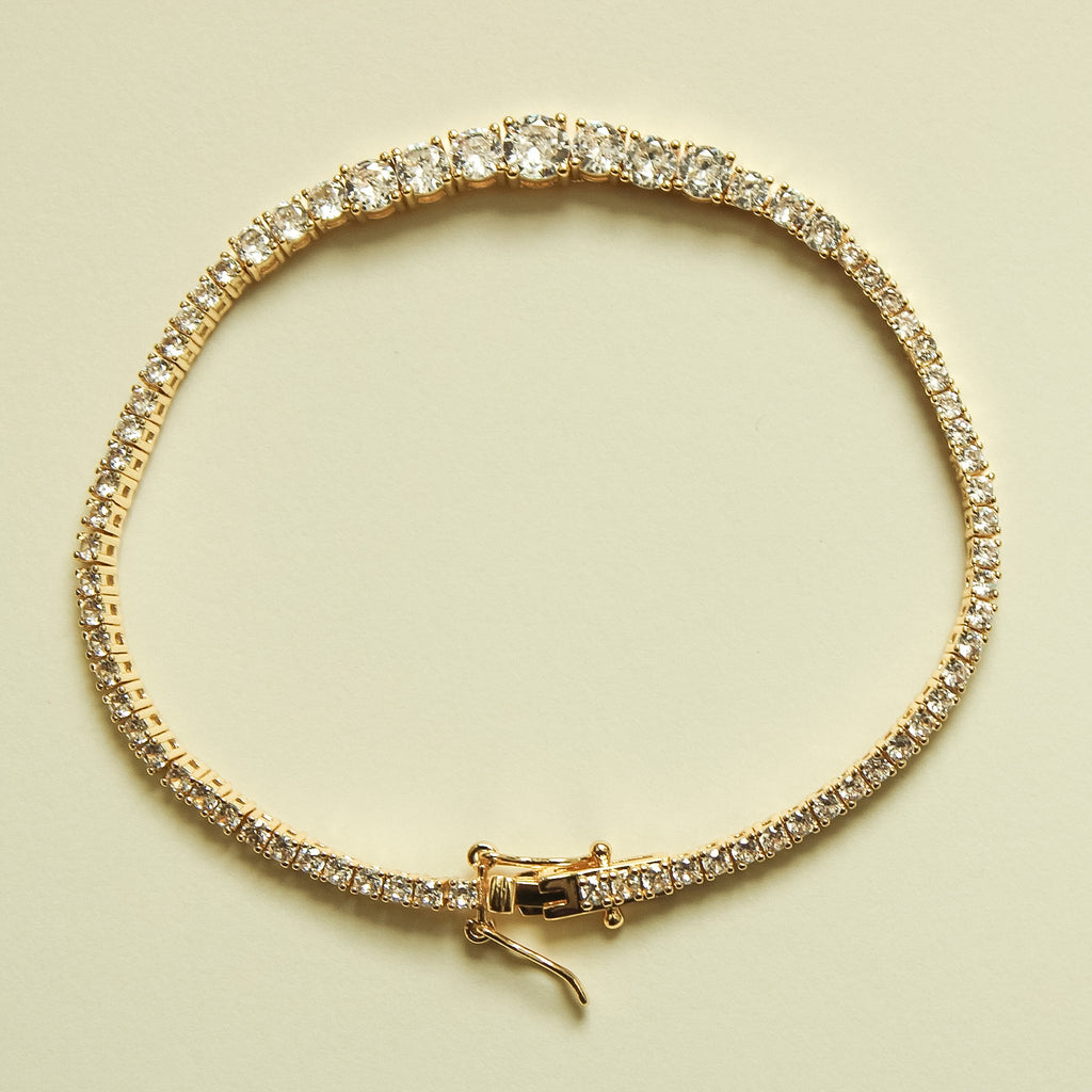 Gold-tone tennis bracelet with graduated clear crystal stones and hook clasp