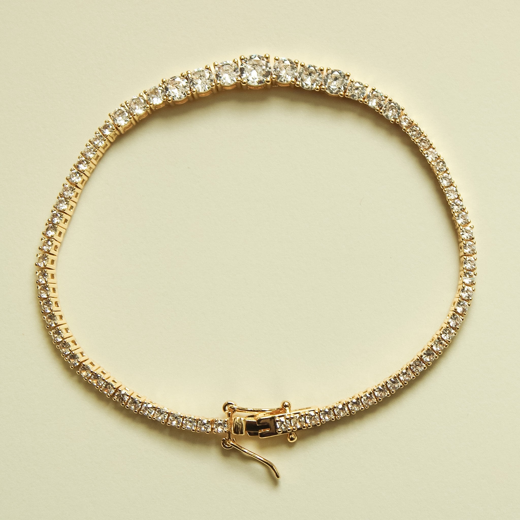 Gold-tone tennis bracelet with graduated clear crystal stones and hook clasp