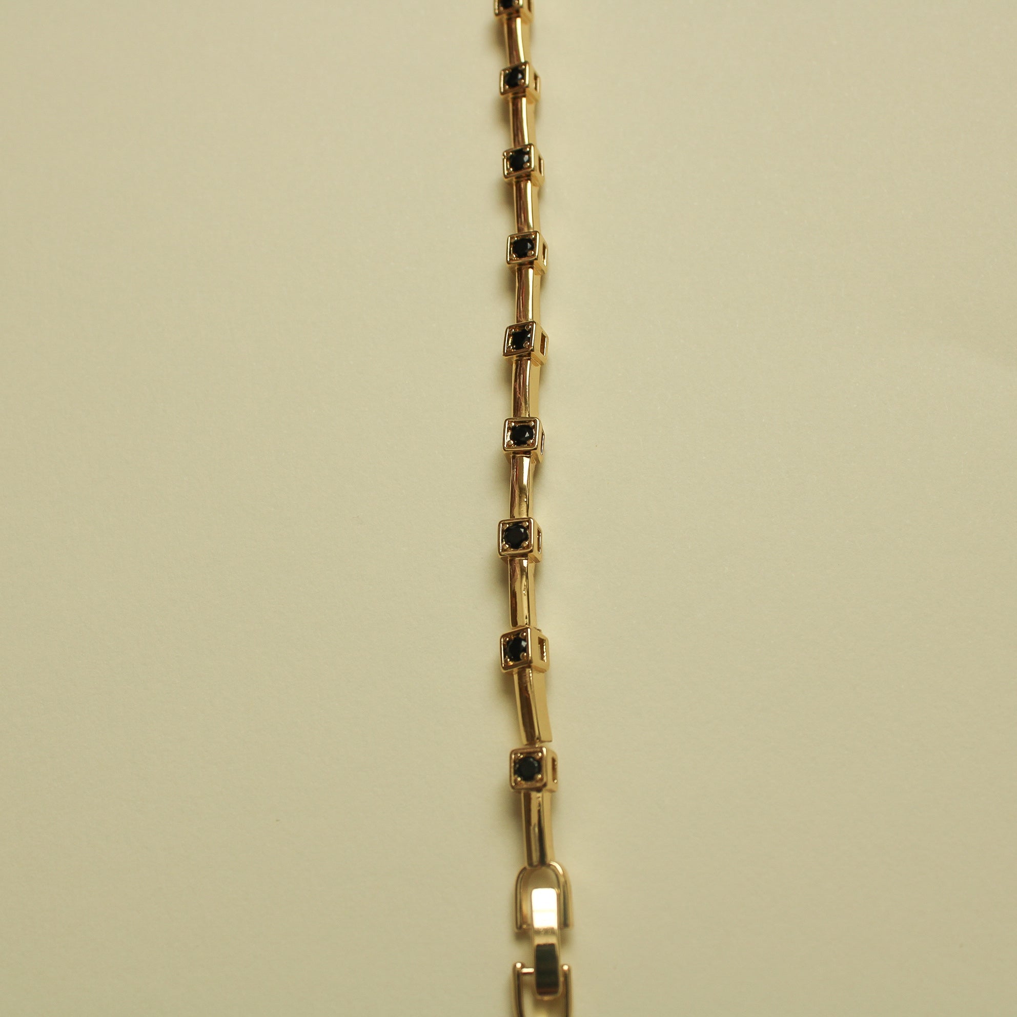 Gold bracelet chain with black CZ bezel stations on rectangular bar links, vertical view