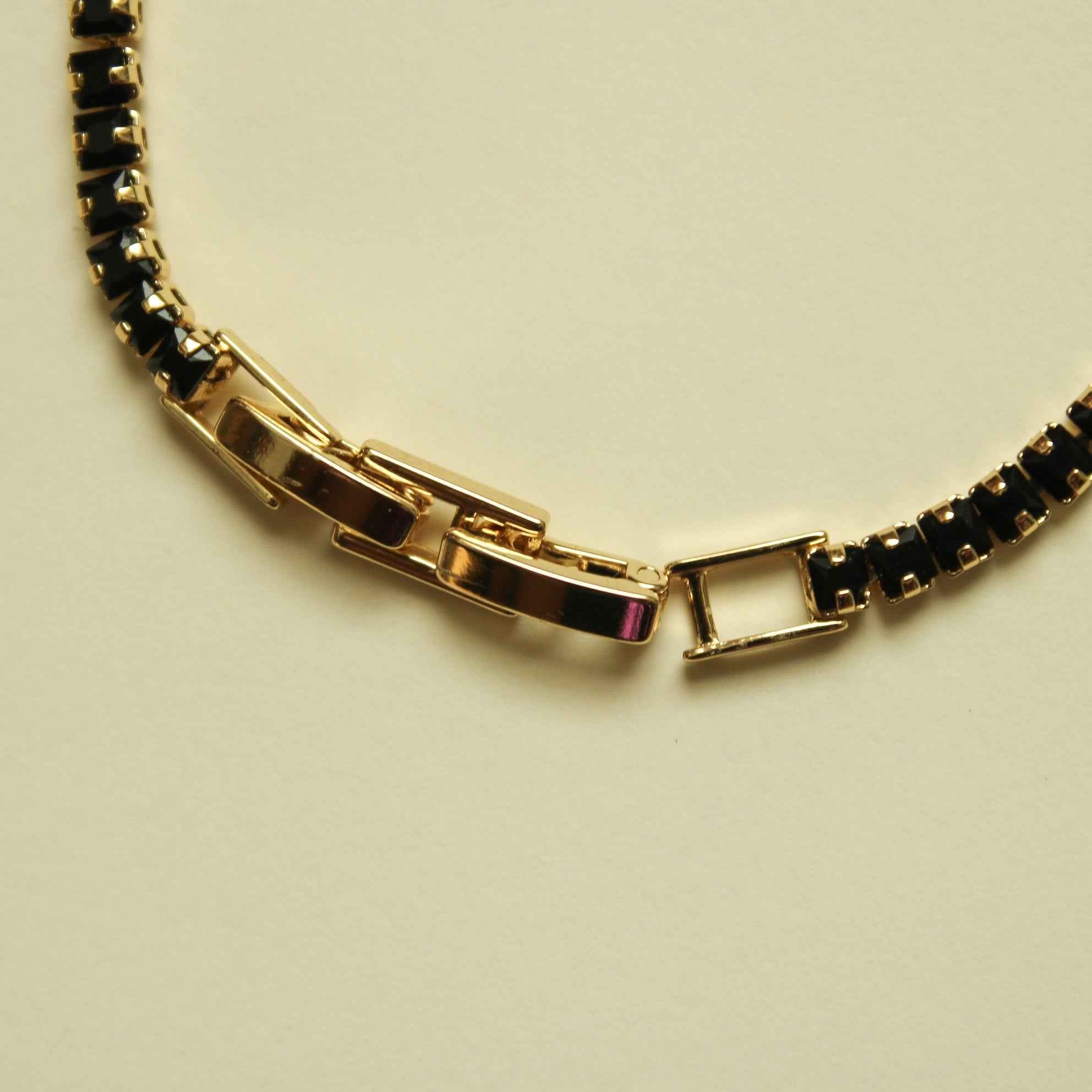Black tennis bracelet with gold bar clasp and black stone bezel links, close-up