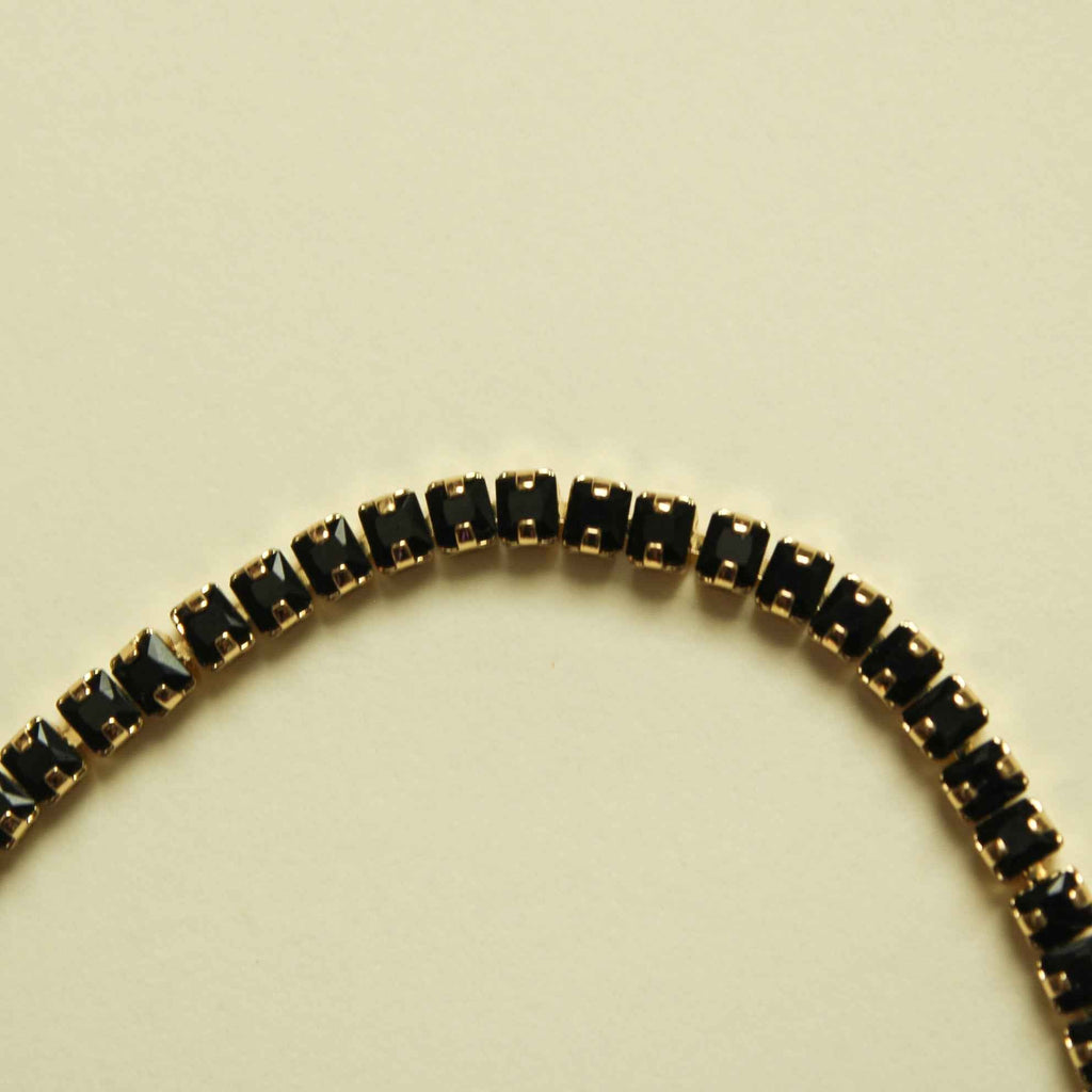 Black tennis bracelet with gold-toned bezel-set stones, full row of sparkling links