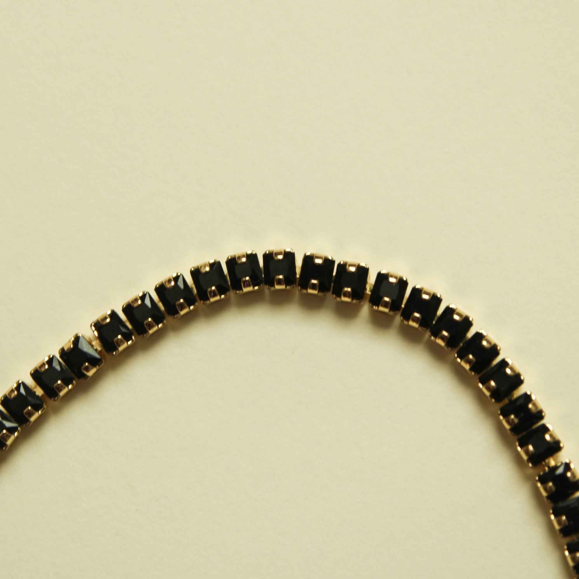 Black tennis bracelet with gold-toned bezel-set stones, full row of sparkling links