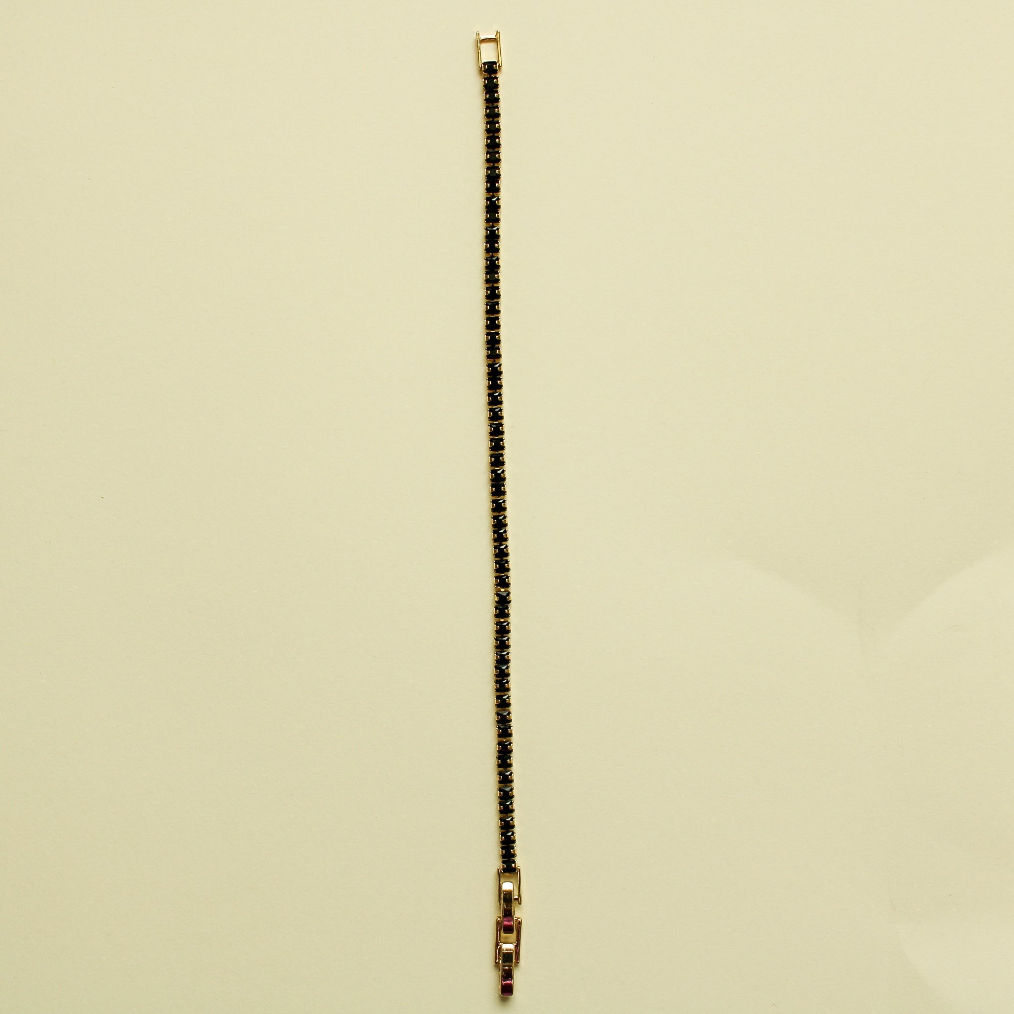 Black tennis bracelet with black stone row and small gold clasp end, vertical