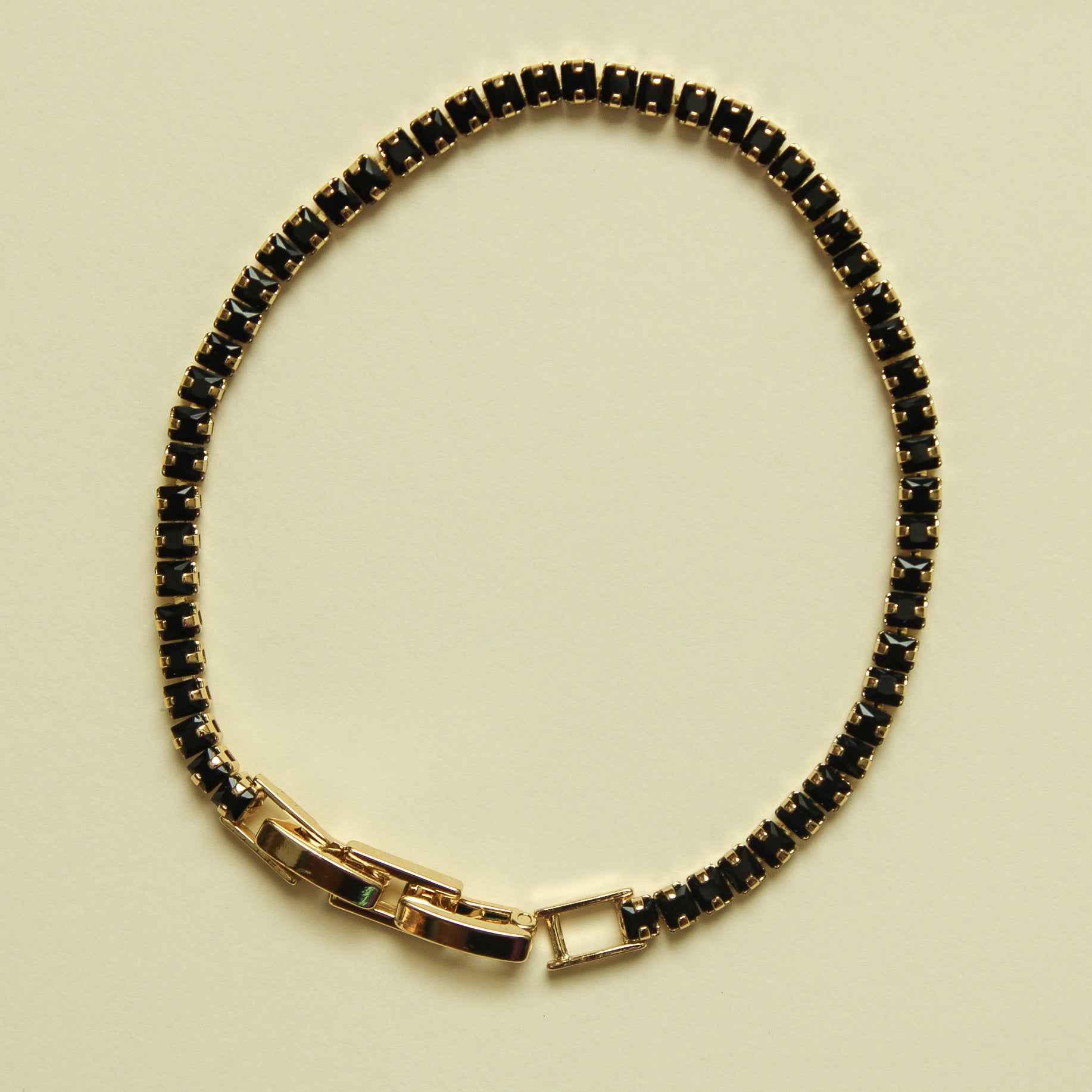 Black tennis bracelet with black stone row and gold-toned bar clasp, full loop