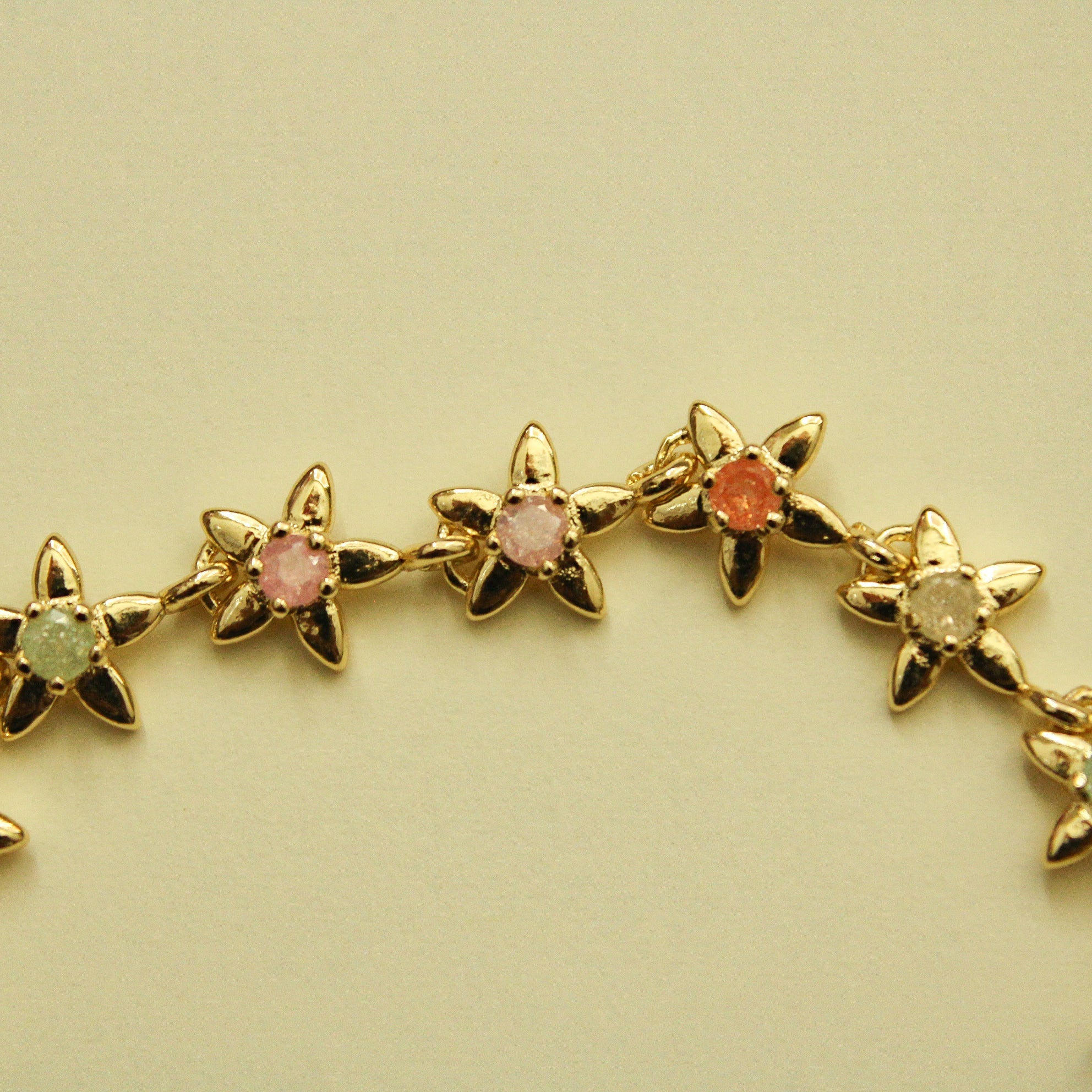Gold flower charm bracelet strand with mixed pink, green, and orange stones.