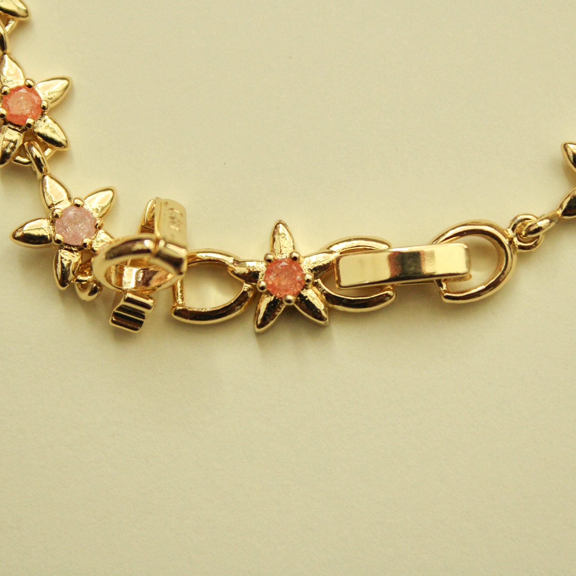 Gold flower charm bracelet with pink and dark green stones, lobster clasp detail.