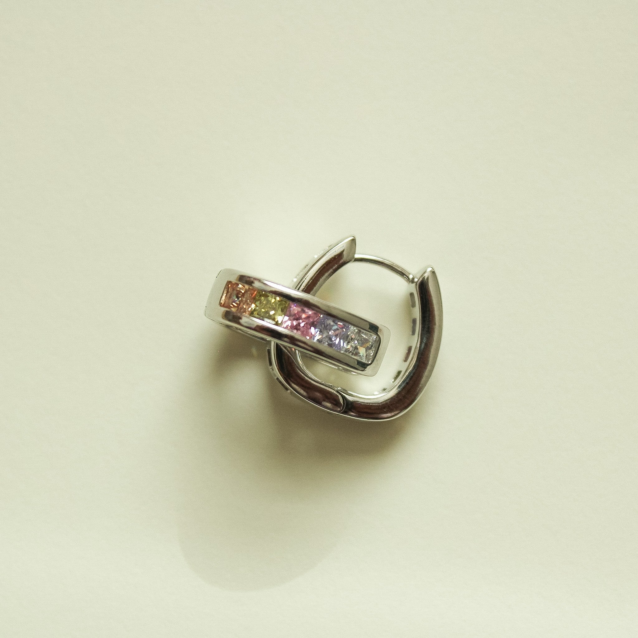 Silver hoop huggie earring with pink center stones and clear bar, angled