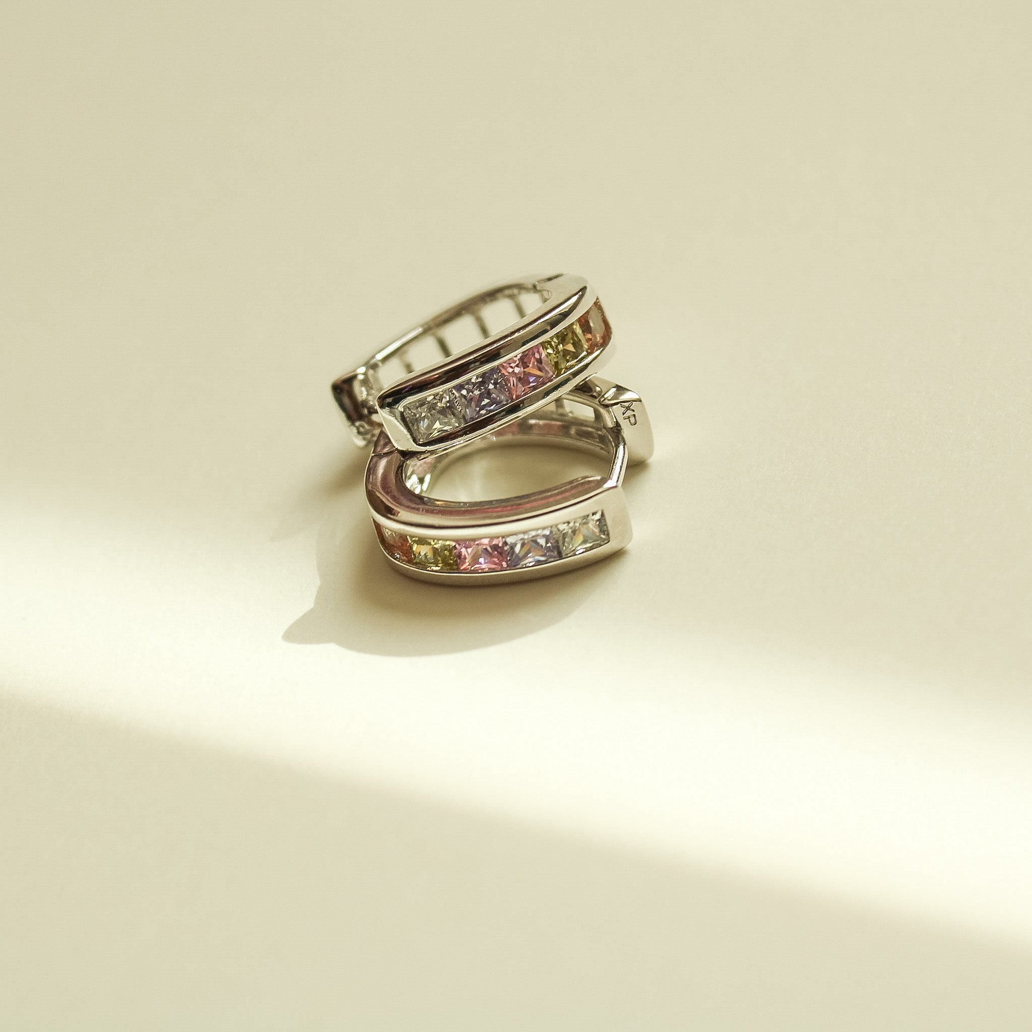 Pair of silver hoop huggie earrings with pink and clear stones, top view