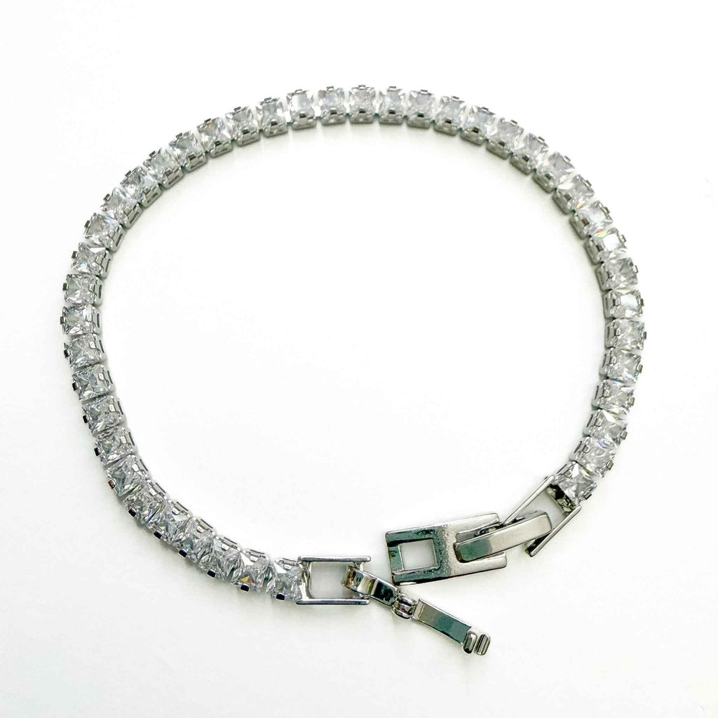 CZ tennis bracelet laid flat with clear stones and green-accent clasp