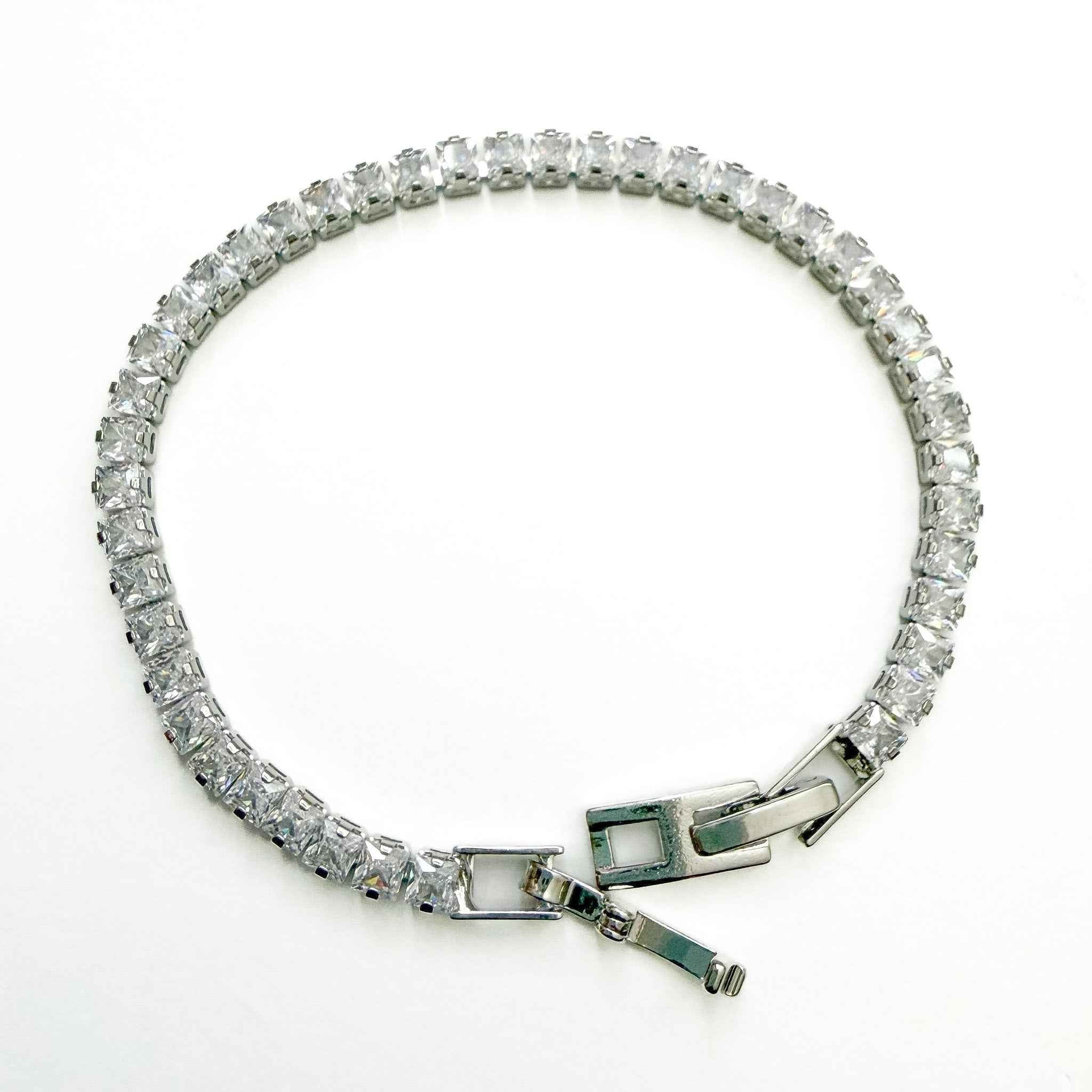 CZ tennis bracelet laid flat with clear stones and green-accent clasp