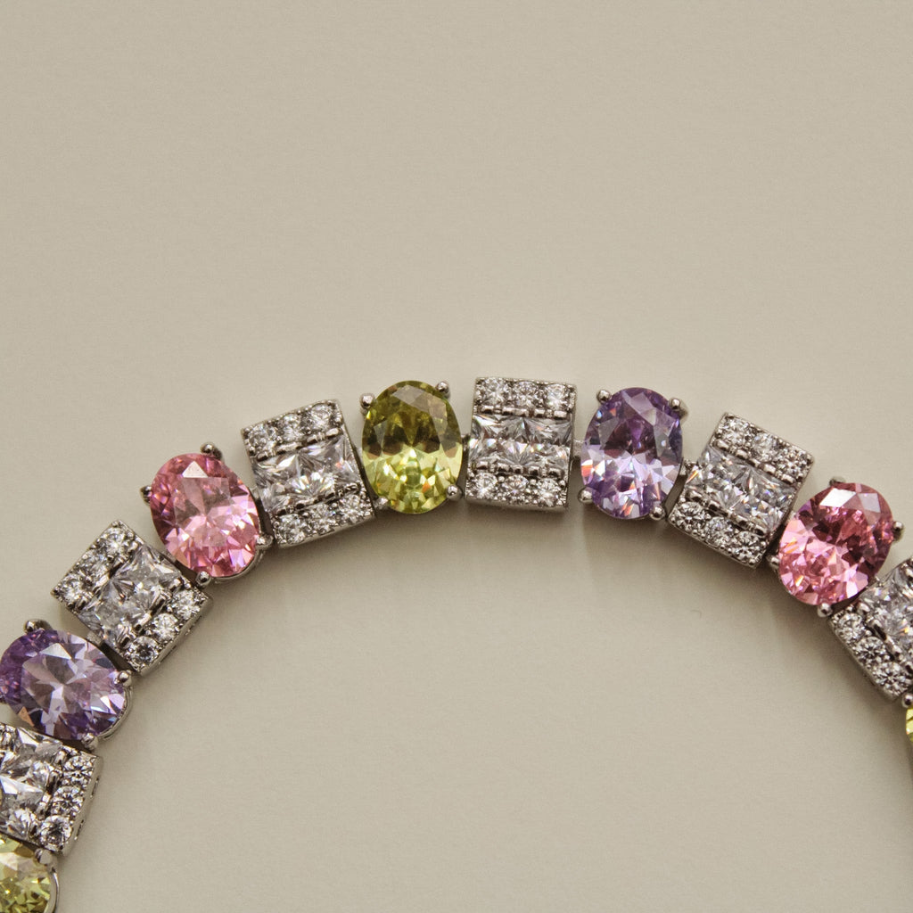Tennis bracelet with round multicolor CZ stones across square pave links, arched view