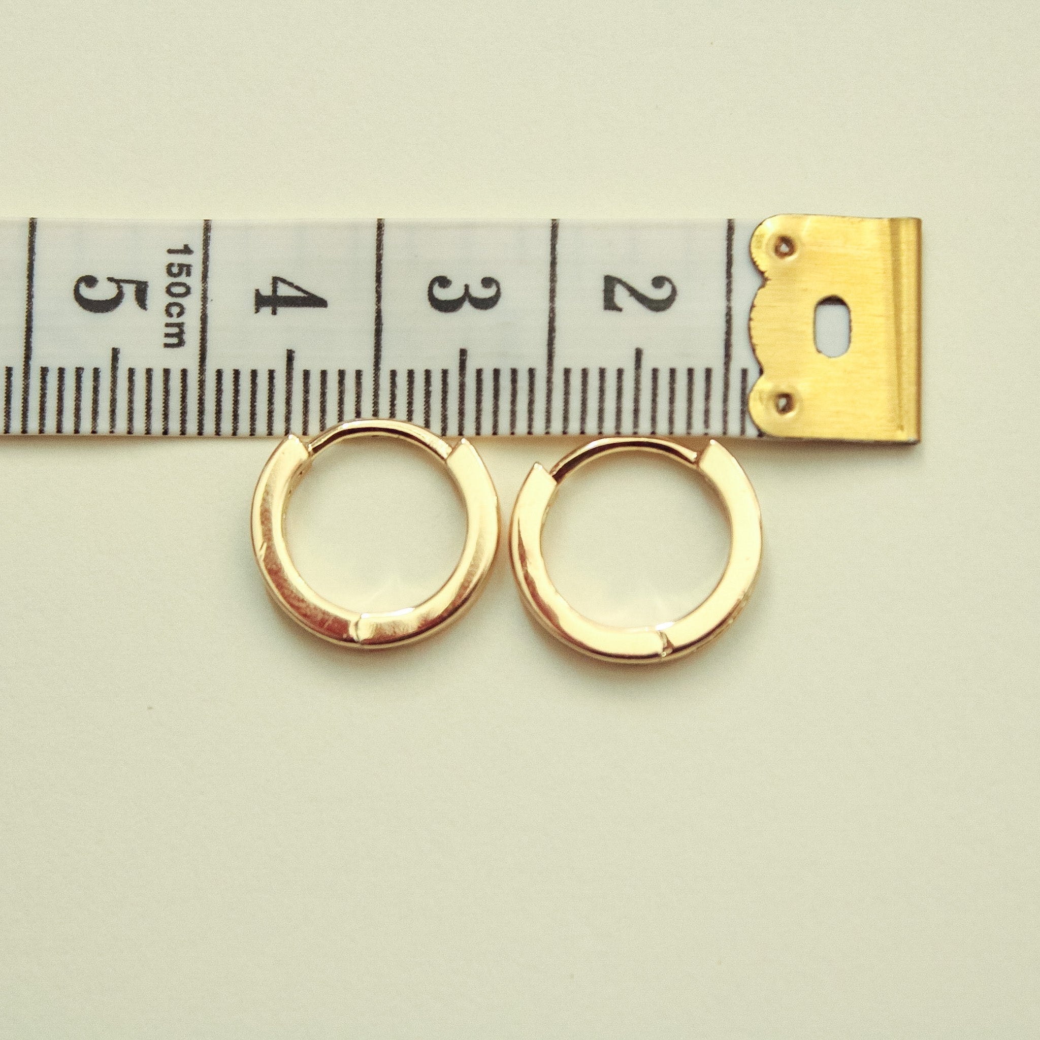 Mini huggie hoop earrings with gold-tone finish; size gauge shows small hoops
