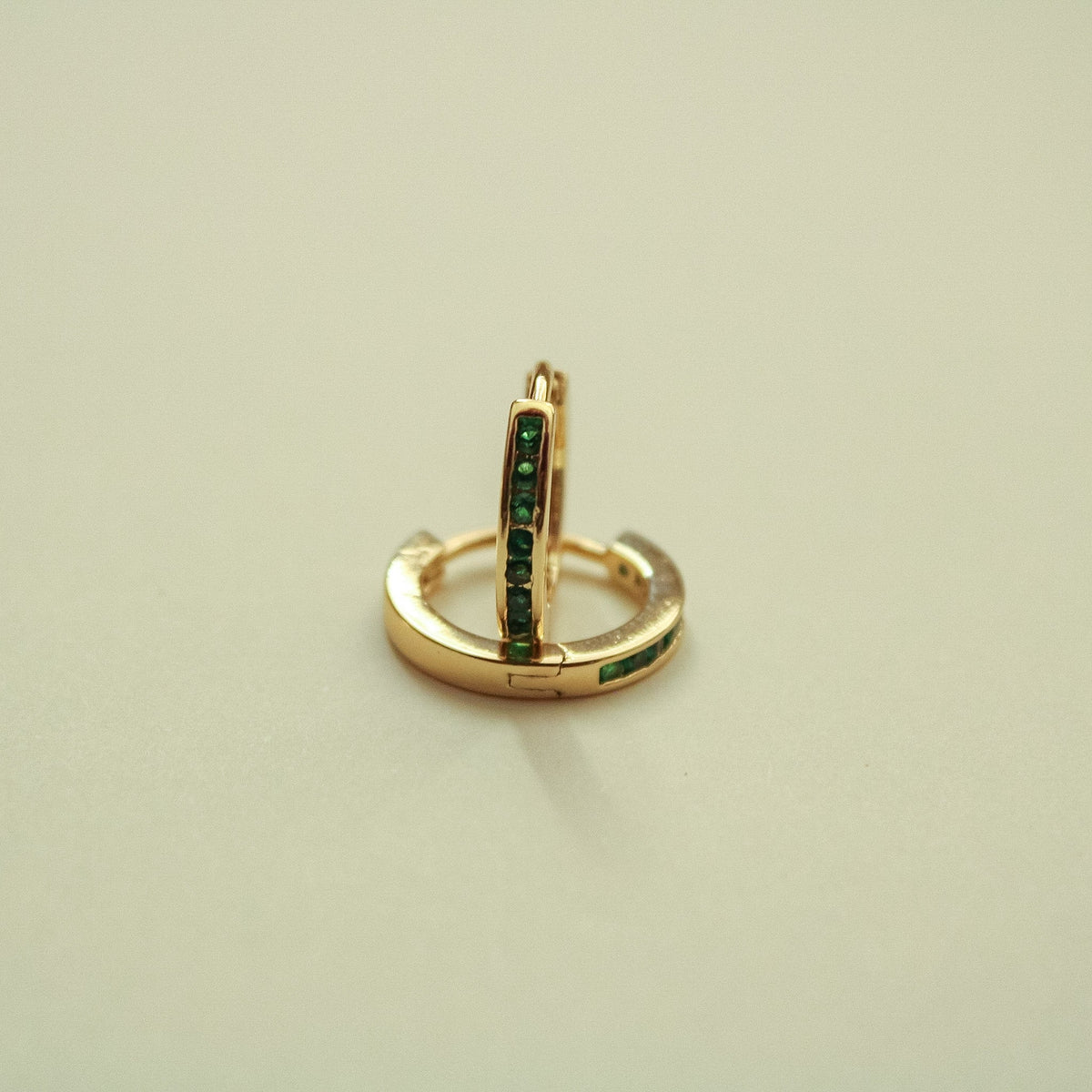 Gold-tone mini huggie hoop earrings with green CZ bar and hinge clasp