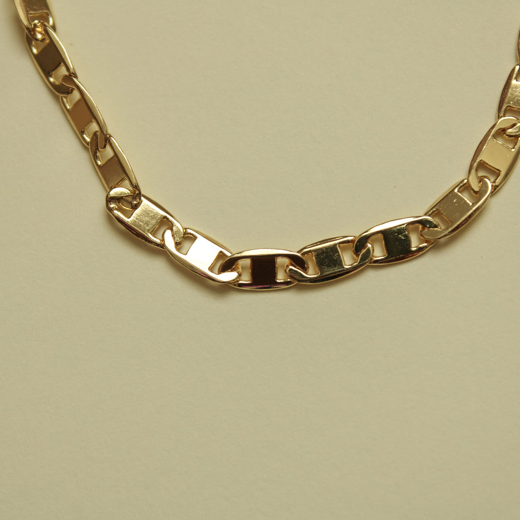 Gold-tone anchor link bracelet with curved chain and interlocking links.