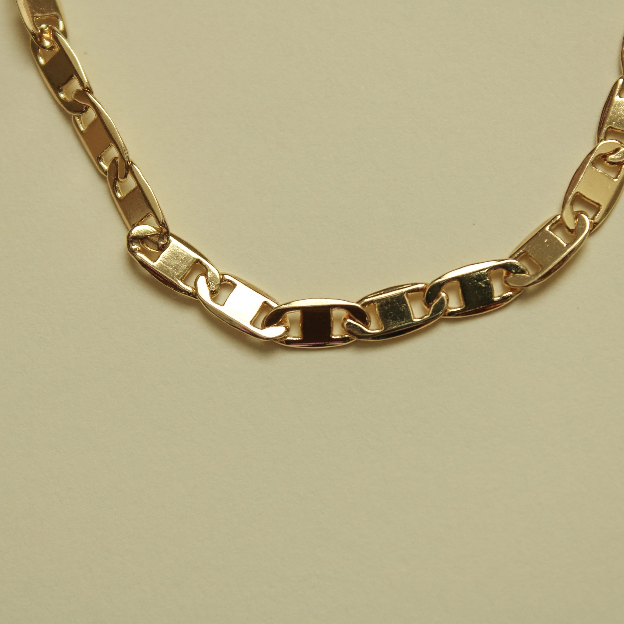 Gold-tone anchor link bracelet with curved chain and interlocking links.