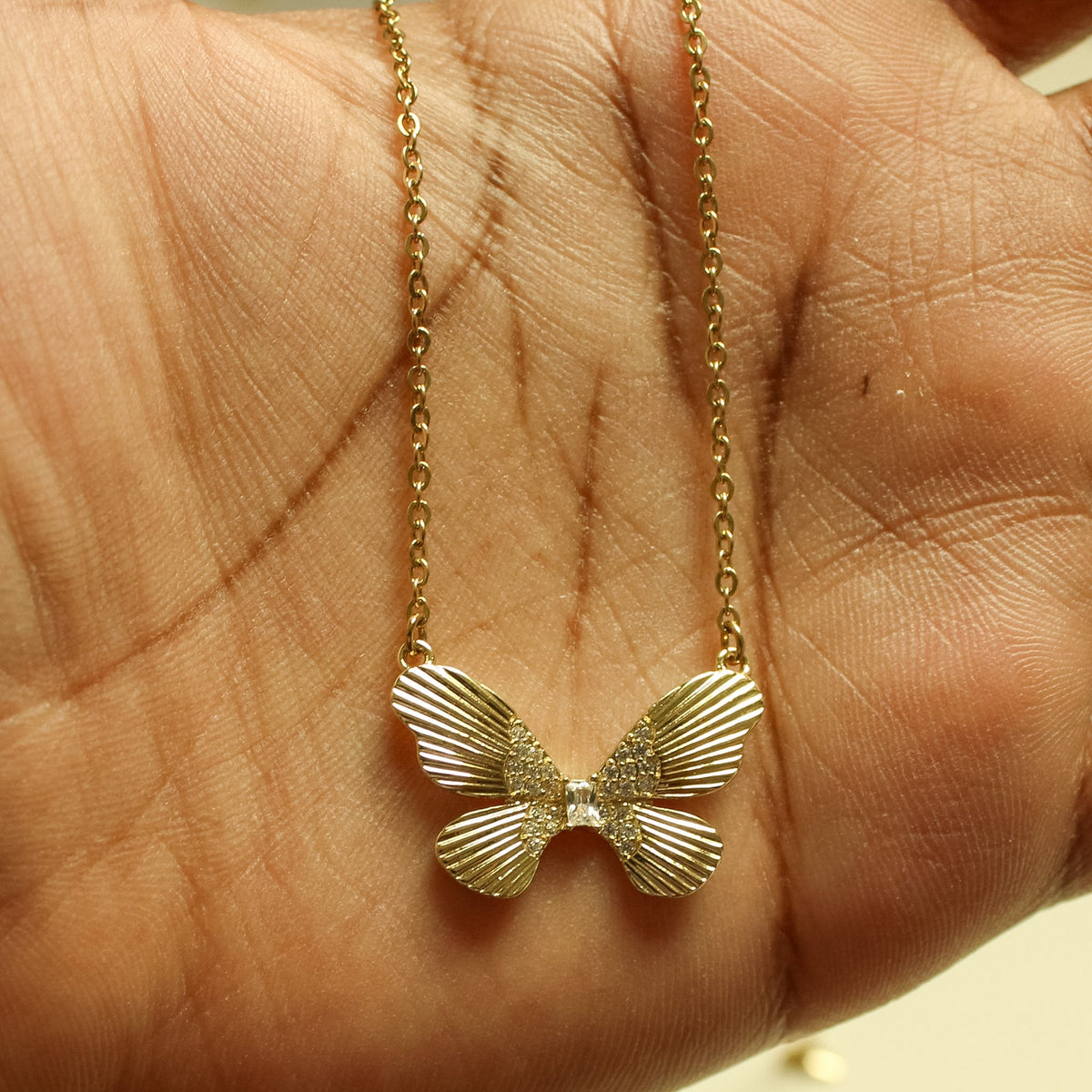 Gold-plated butterfly CZ necklace on hand, fluted wings detail close-up.