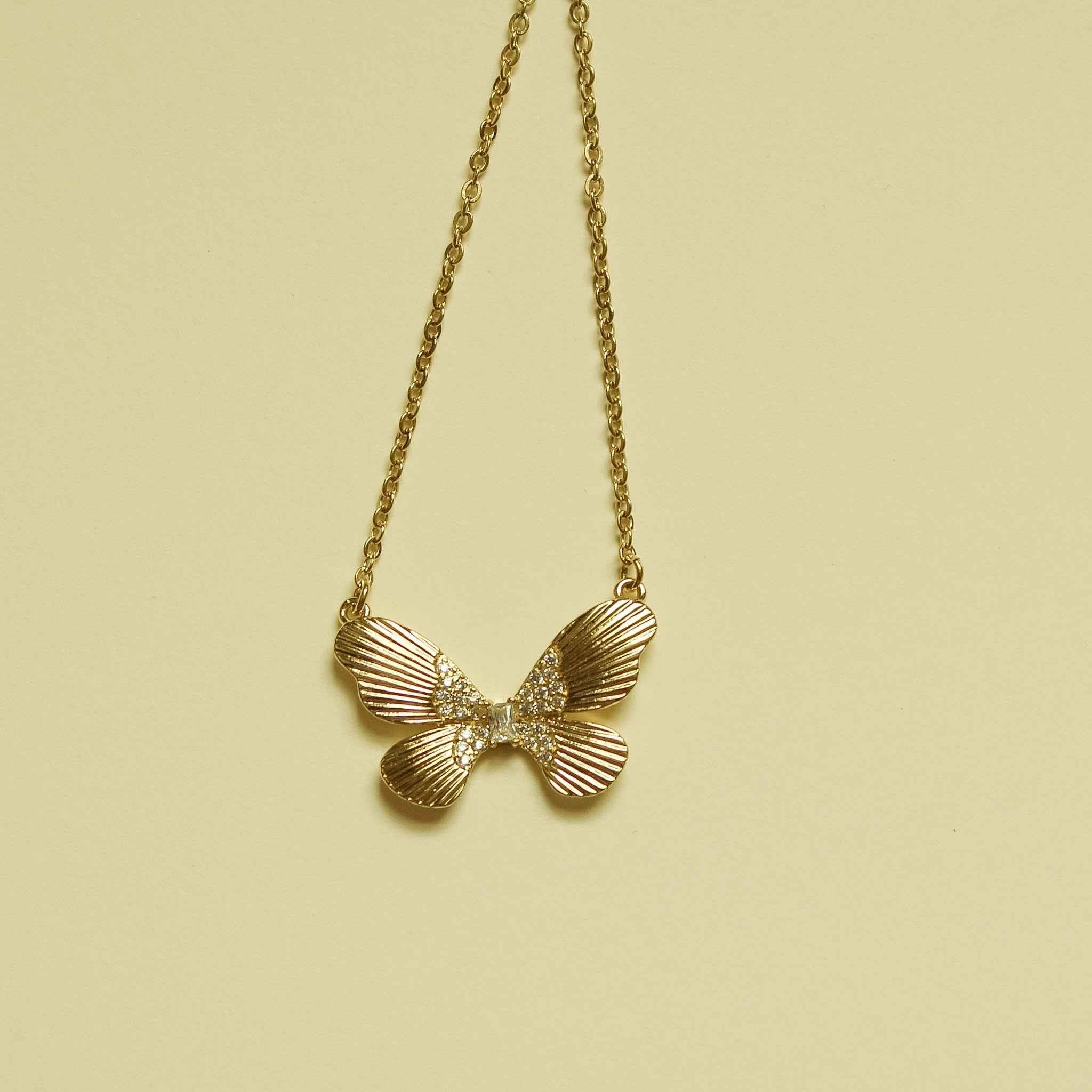 Gold-plated butterfly CZ necklace with three fluted wings, hanging on chain.