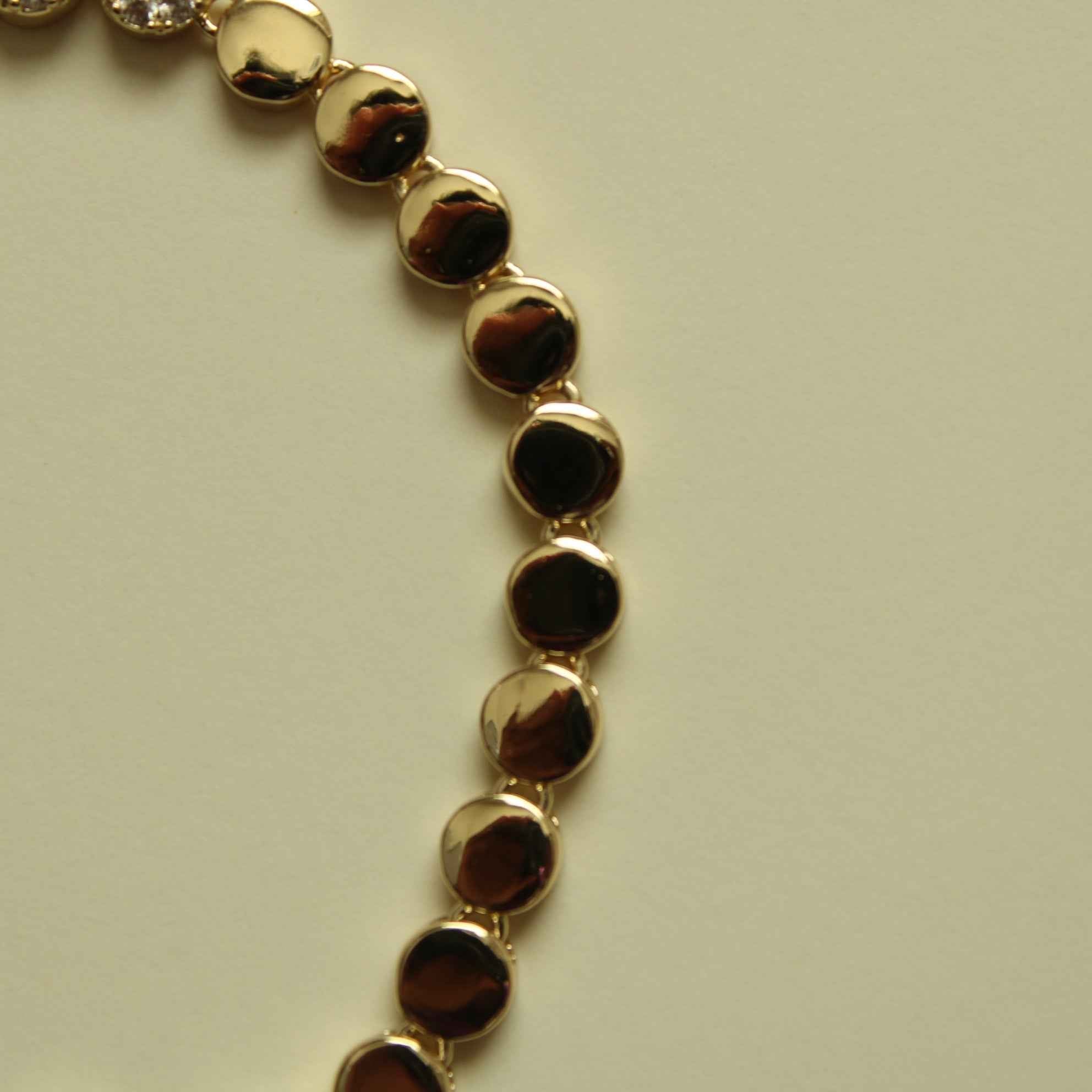Gold disc tennis bracelet with glossy round links along a bracelet chain.