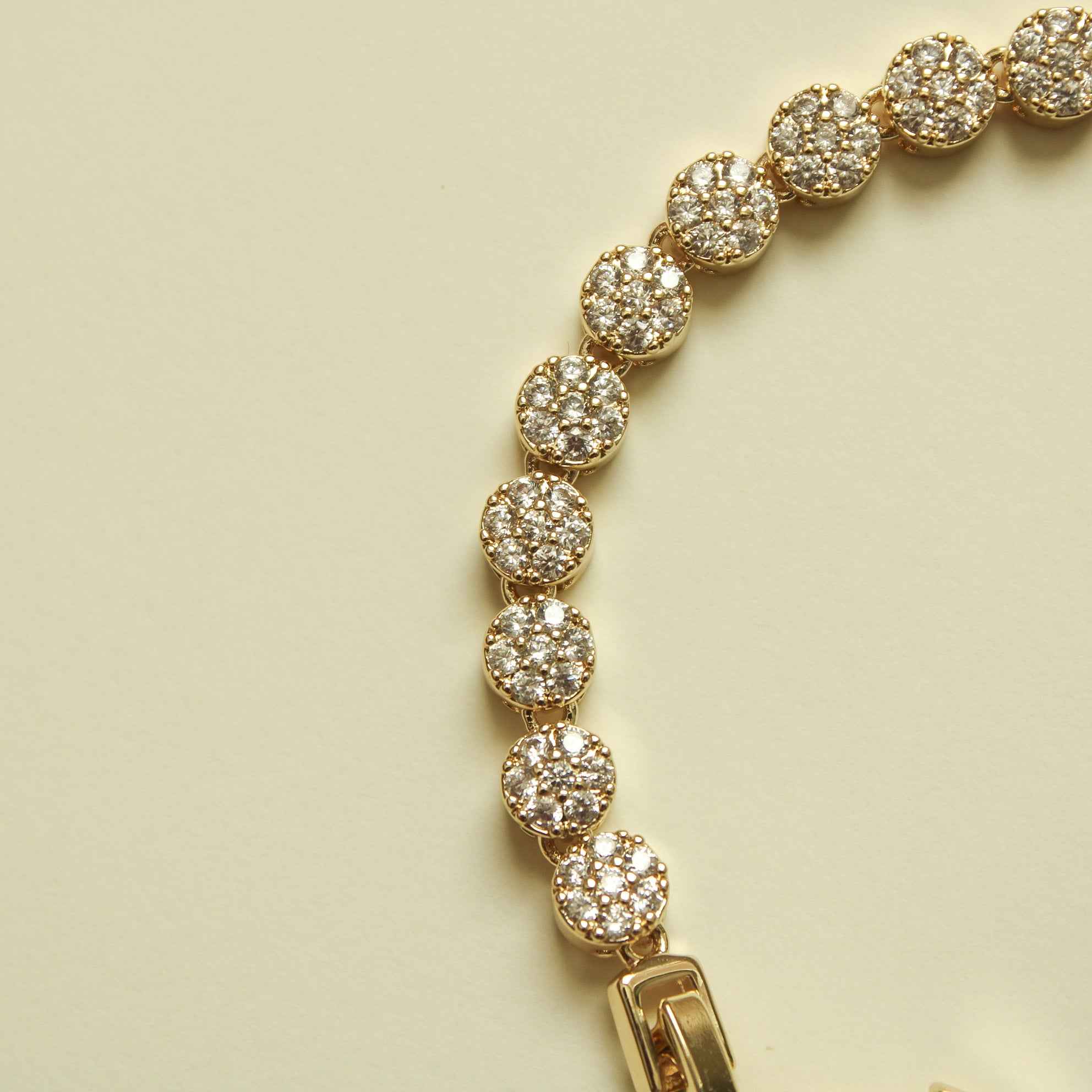Round pavé stone stations on a gold tennis bracelet with a bar clasp.