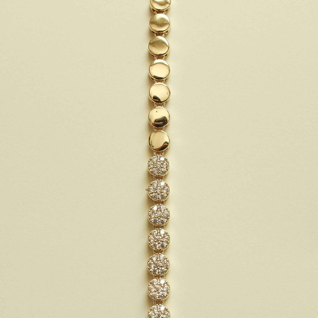 Pavé tennis bracelet strand with round pavé stations and gold disc links at top.