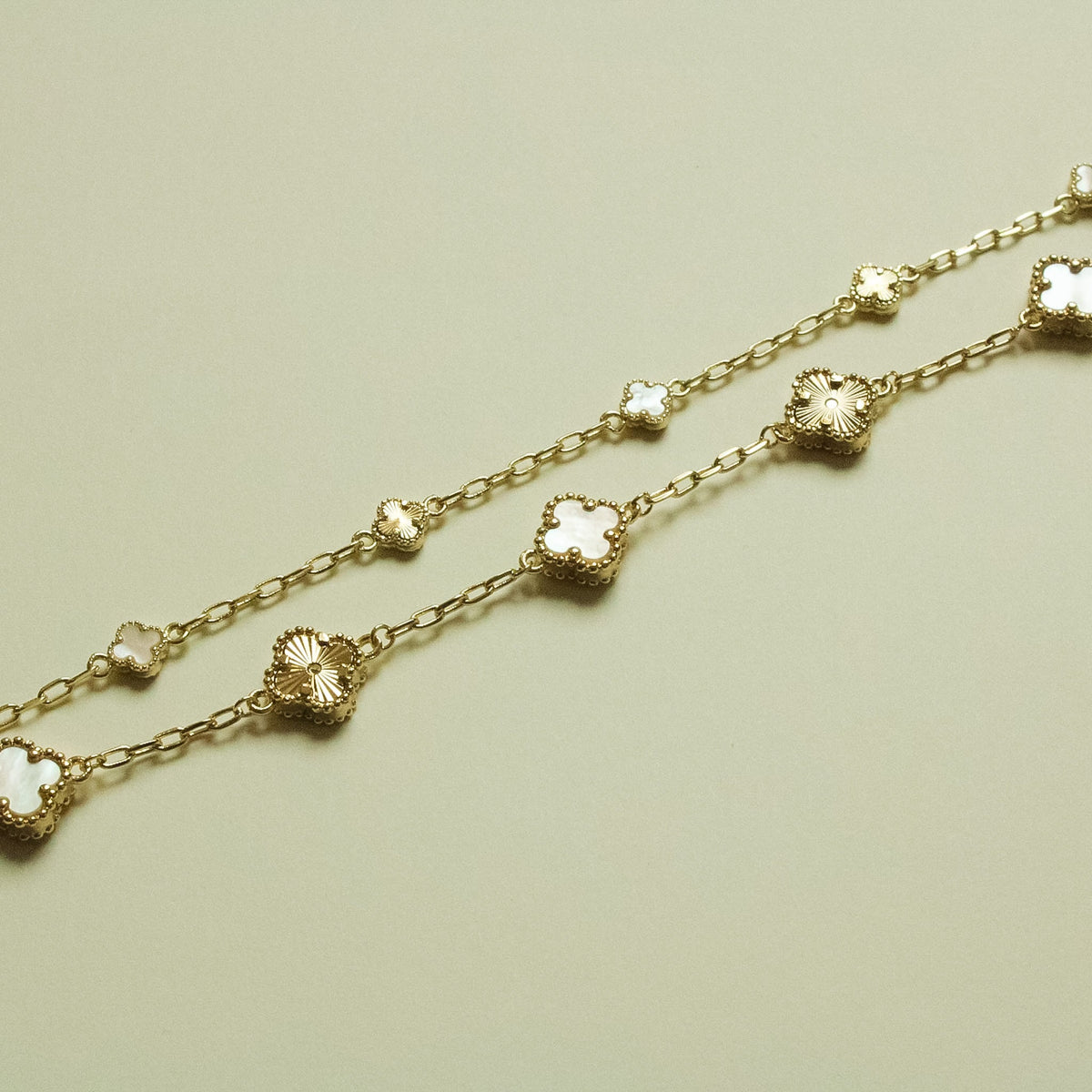 Gold bracelet strand with small clover charms and mother-of-pearl inlays