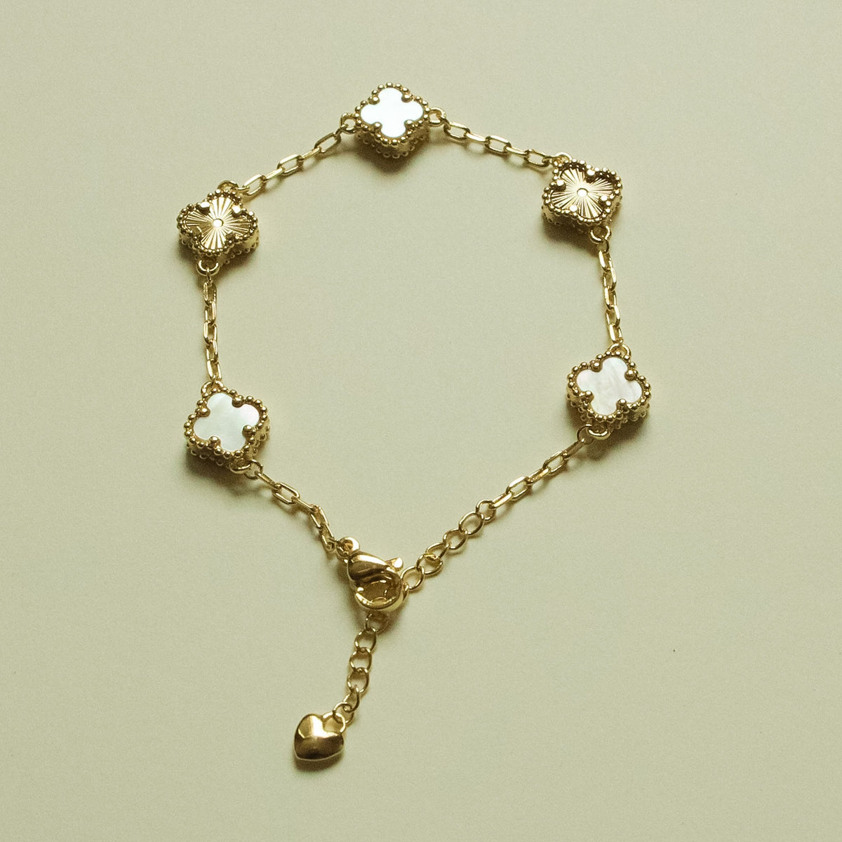 Gold-tone bracelet with clover charms, heart drop, and mother-of-pearl inlay