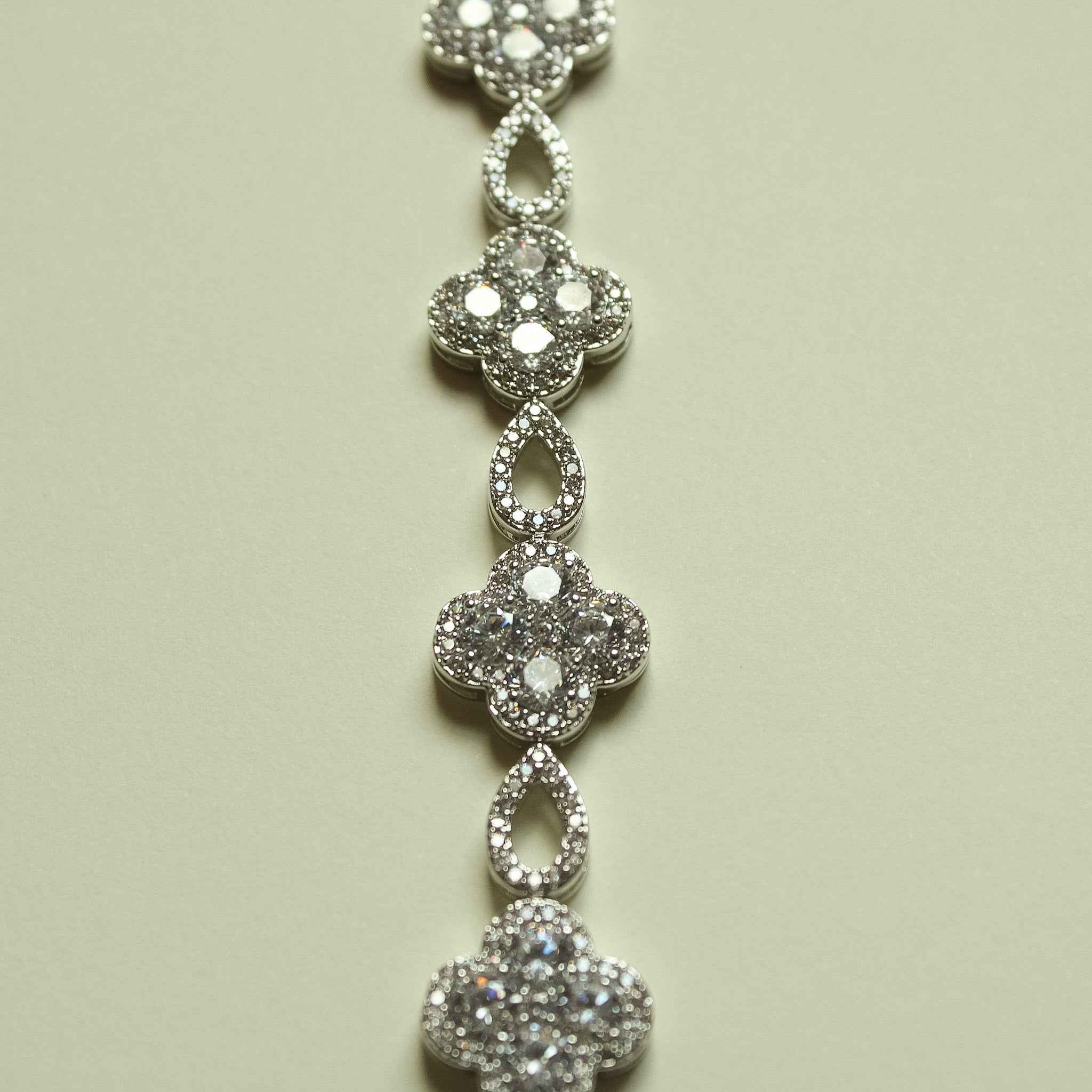 Vertical view of silver-tone CZ clover charms connected by teardrop links