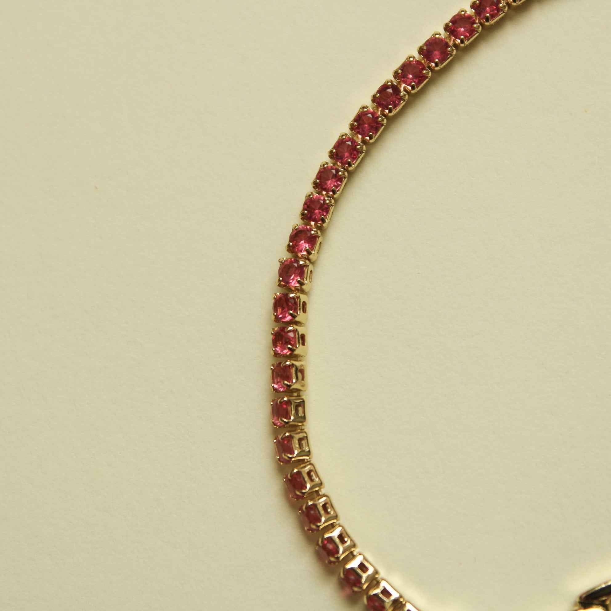 Gold-tone tennis bracelet detail with pink CZ pavé links along the curved chain.