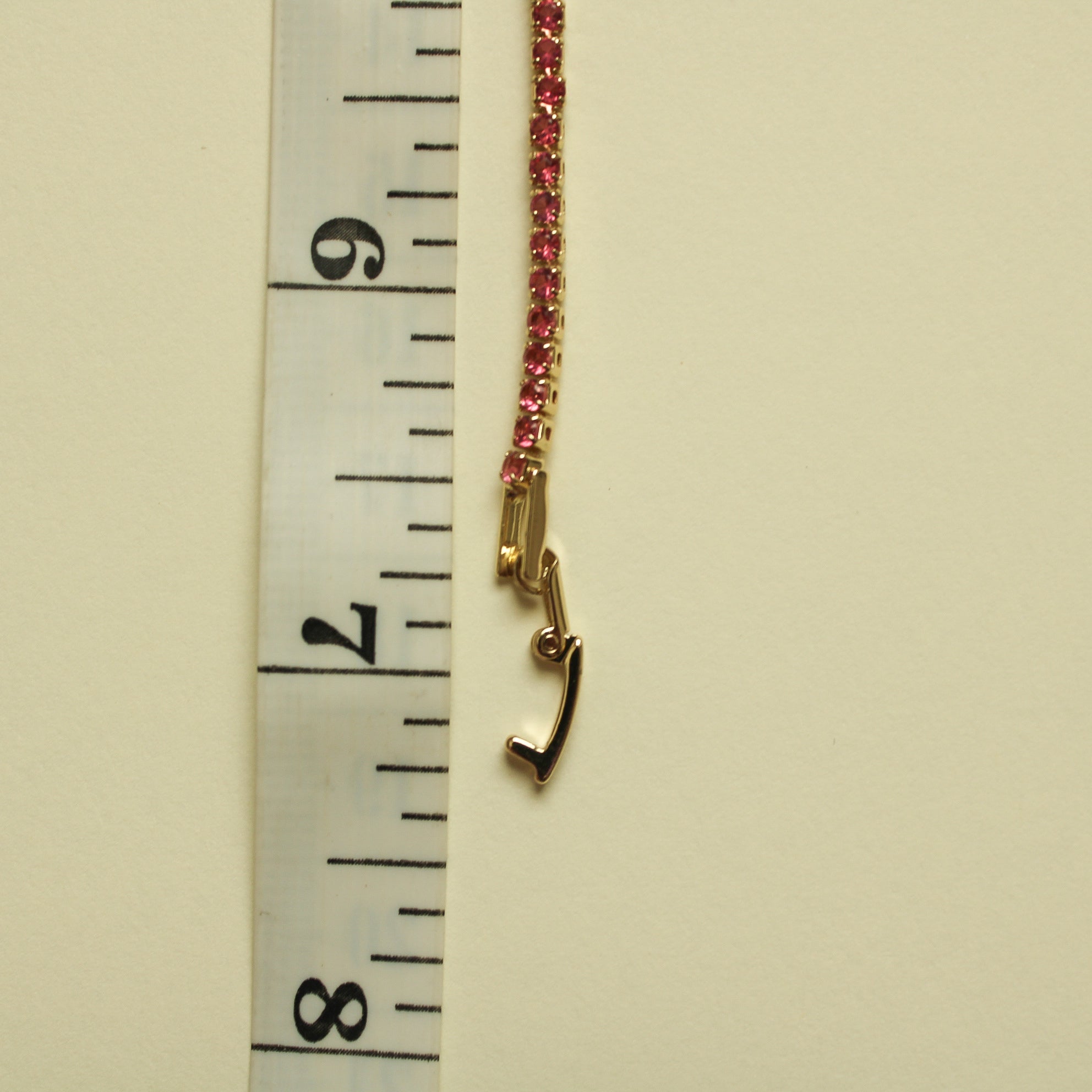 Gold-tone bracelet with a pink CZ row and small clasp hook at the end.