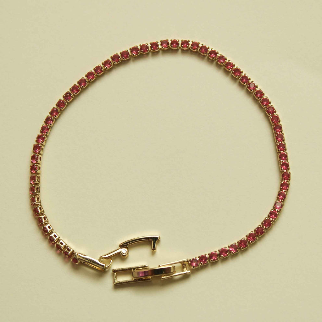 Gold-tone tennis bracelet with pink CZ stones and a rectangular clasp at center.