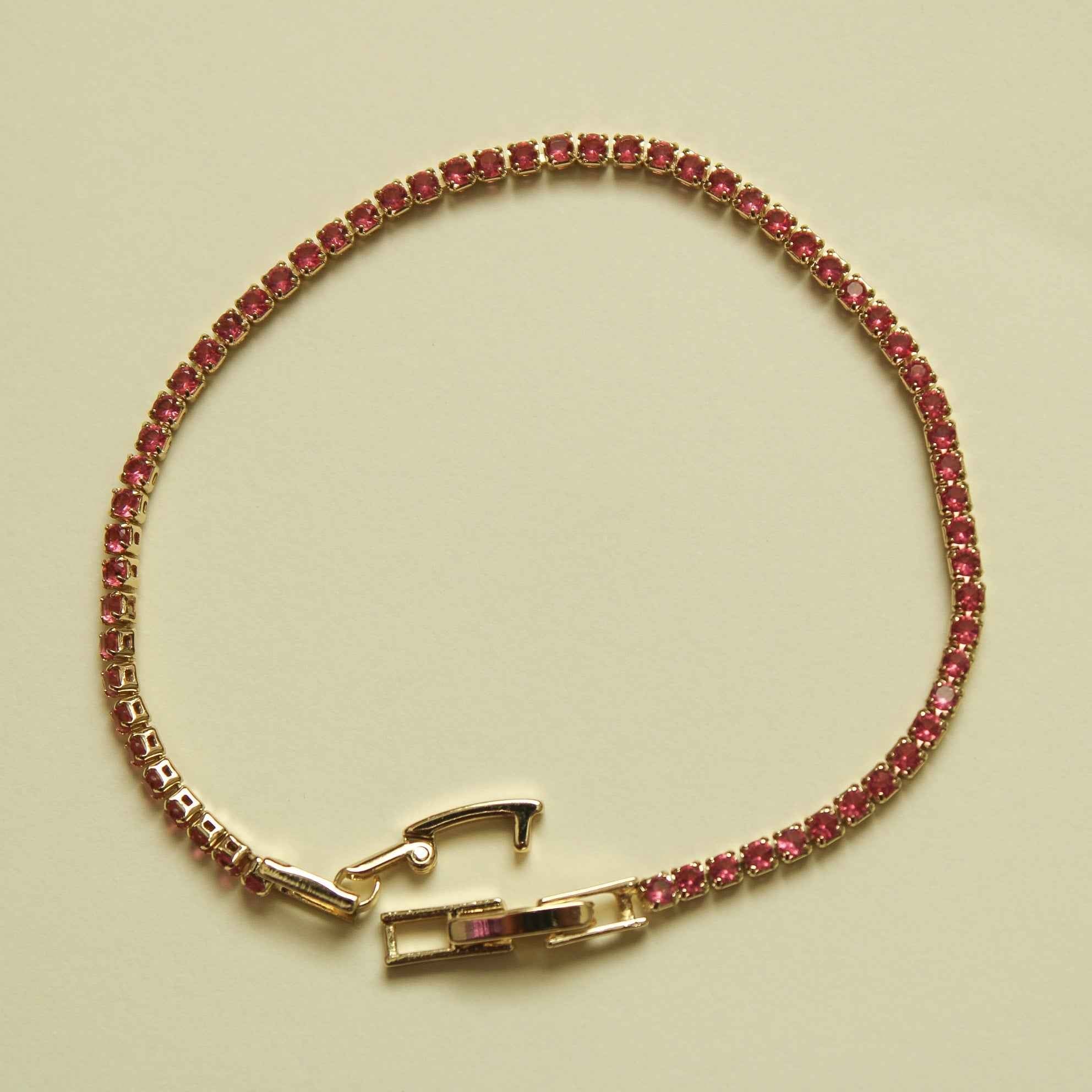 Gold-tone tennis bracelet with pink CZ stones and a rectangular clasp at center.