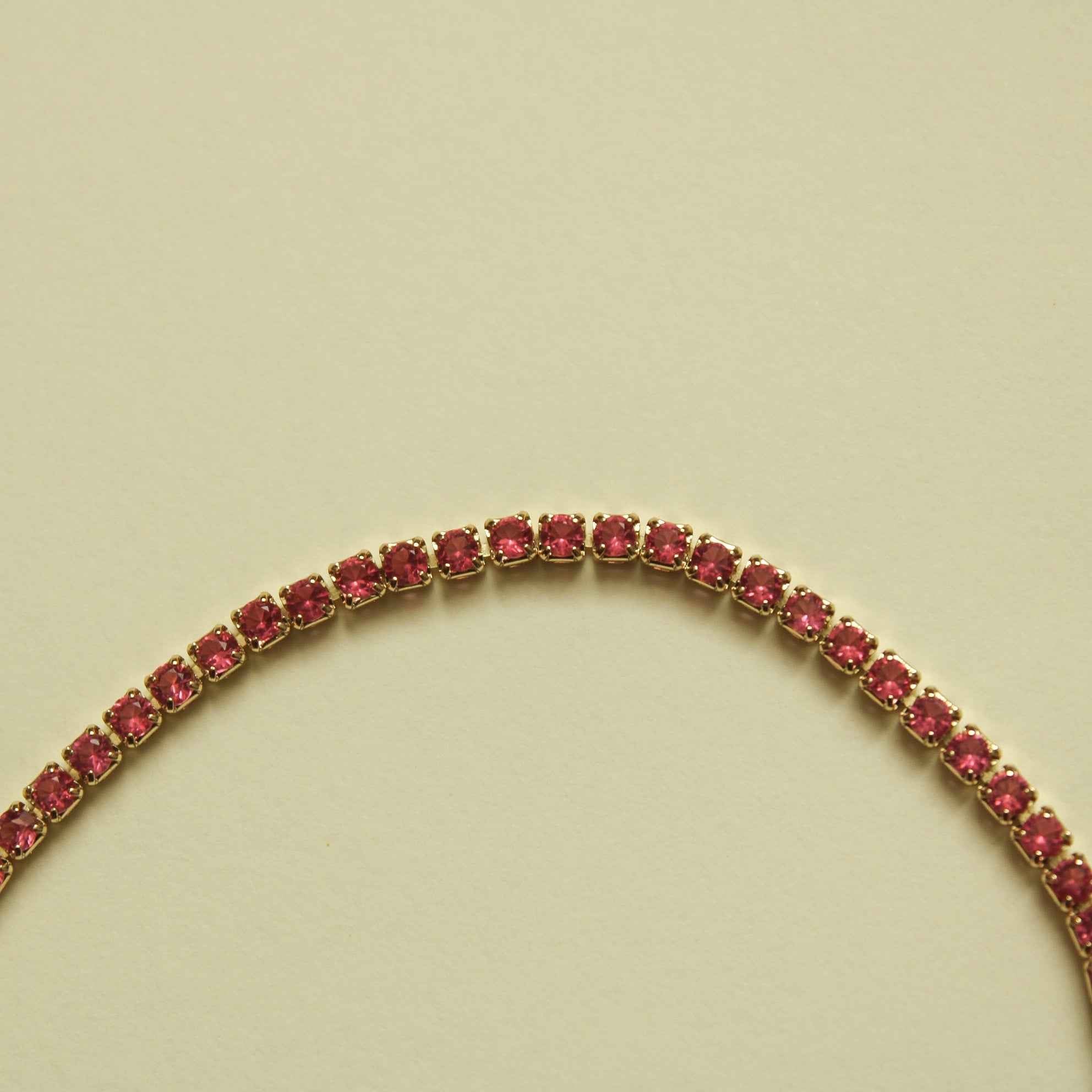 Pink CZ stone row on a gold-tone tennis bracelet, close-up of linked stones.