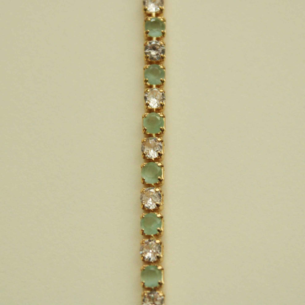 Gold-tone tennis bracelet detail with seafoam green stones and clear CZ pavé links