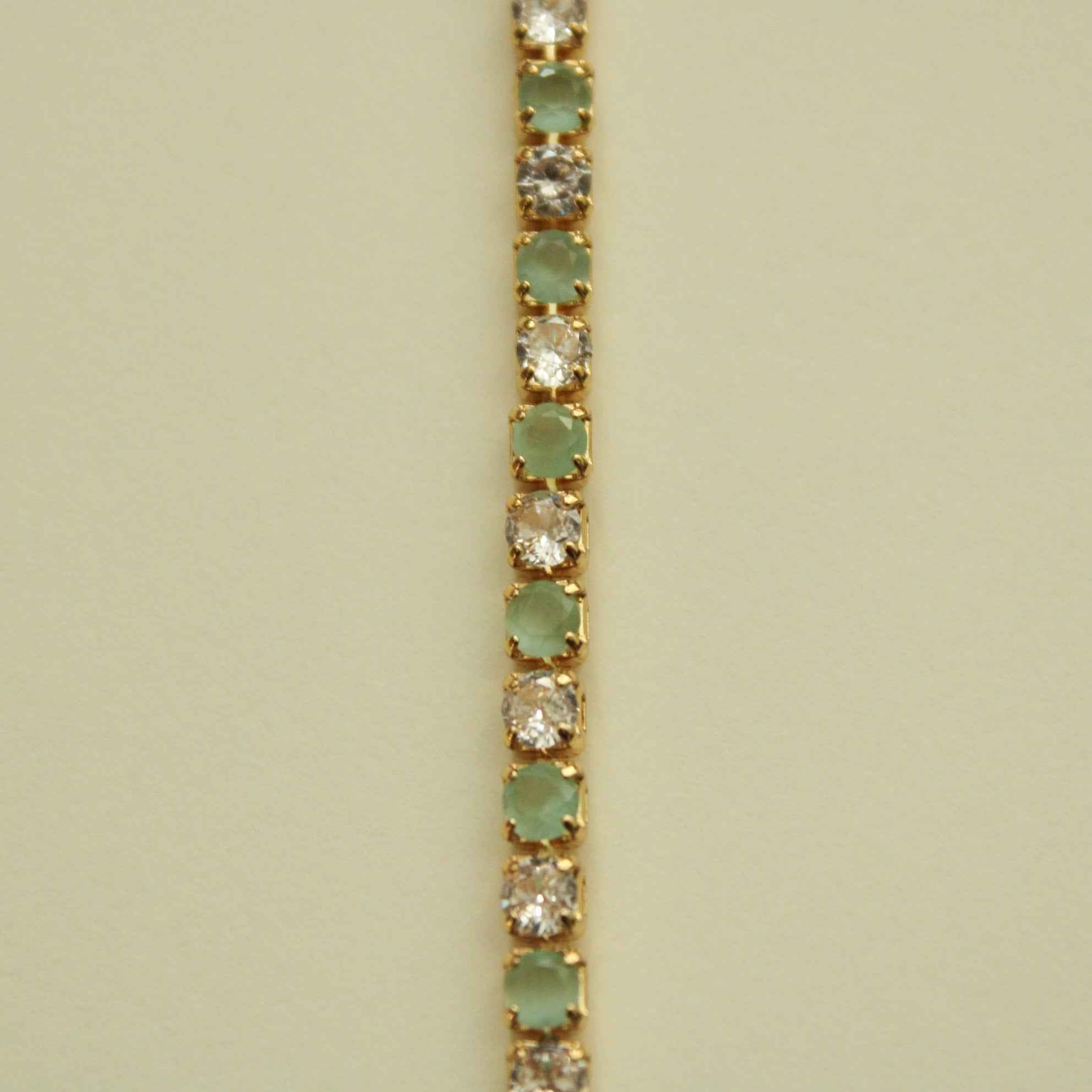 Gold-tone tennis bracelet detail with seafoam green stones and clear CZ pavé links