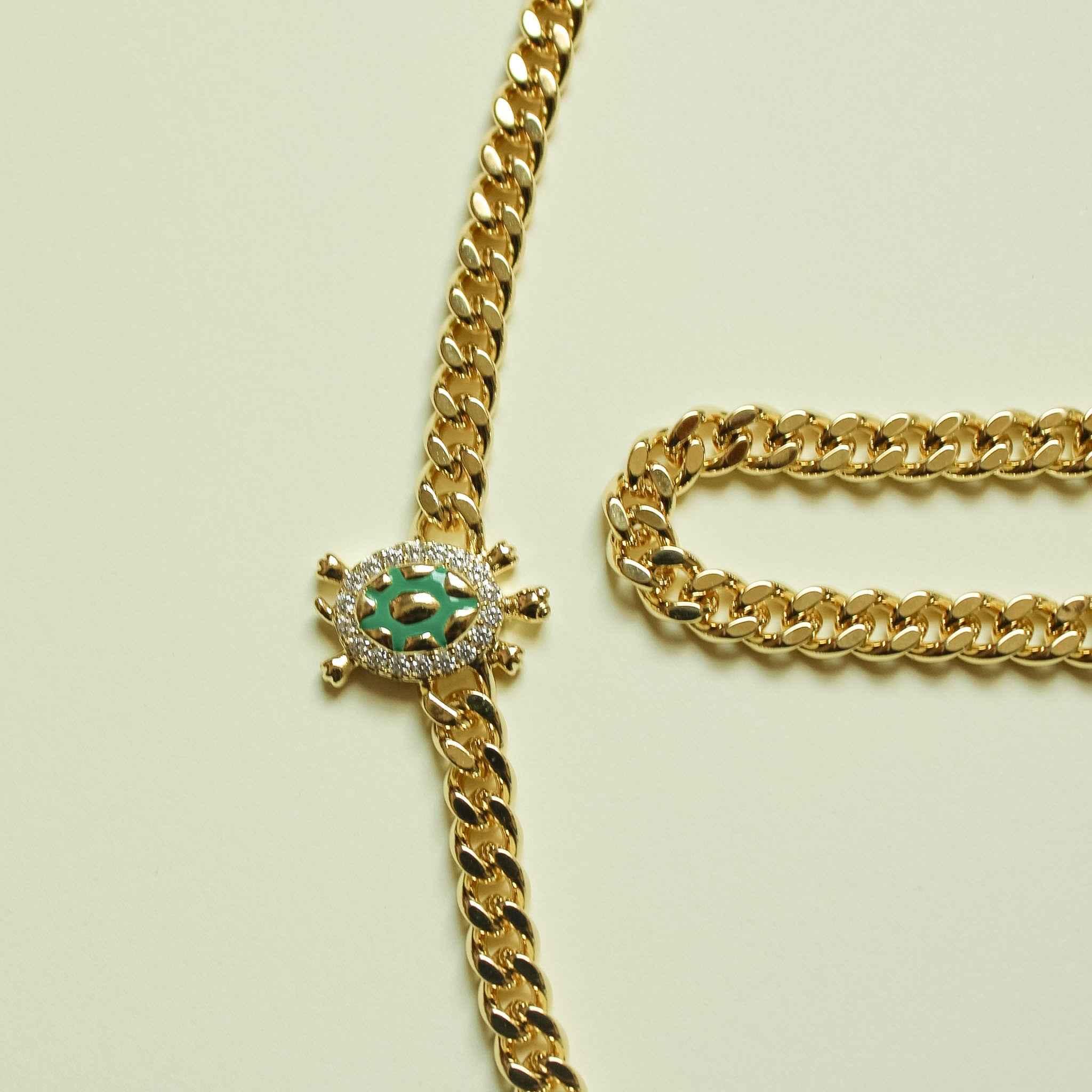 Gold turtle charm detail on Cuban chain, with green and clear stone accents